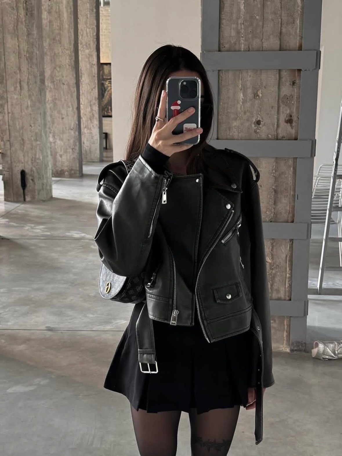 A person wearing a black leather biker jacket and black skirt taking a mirror selfie.
