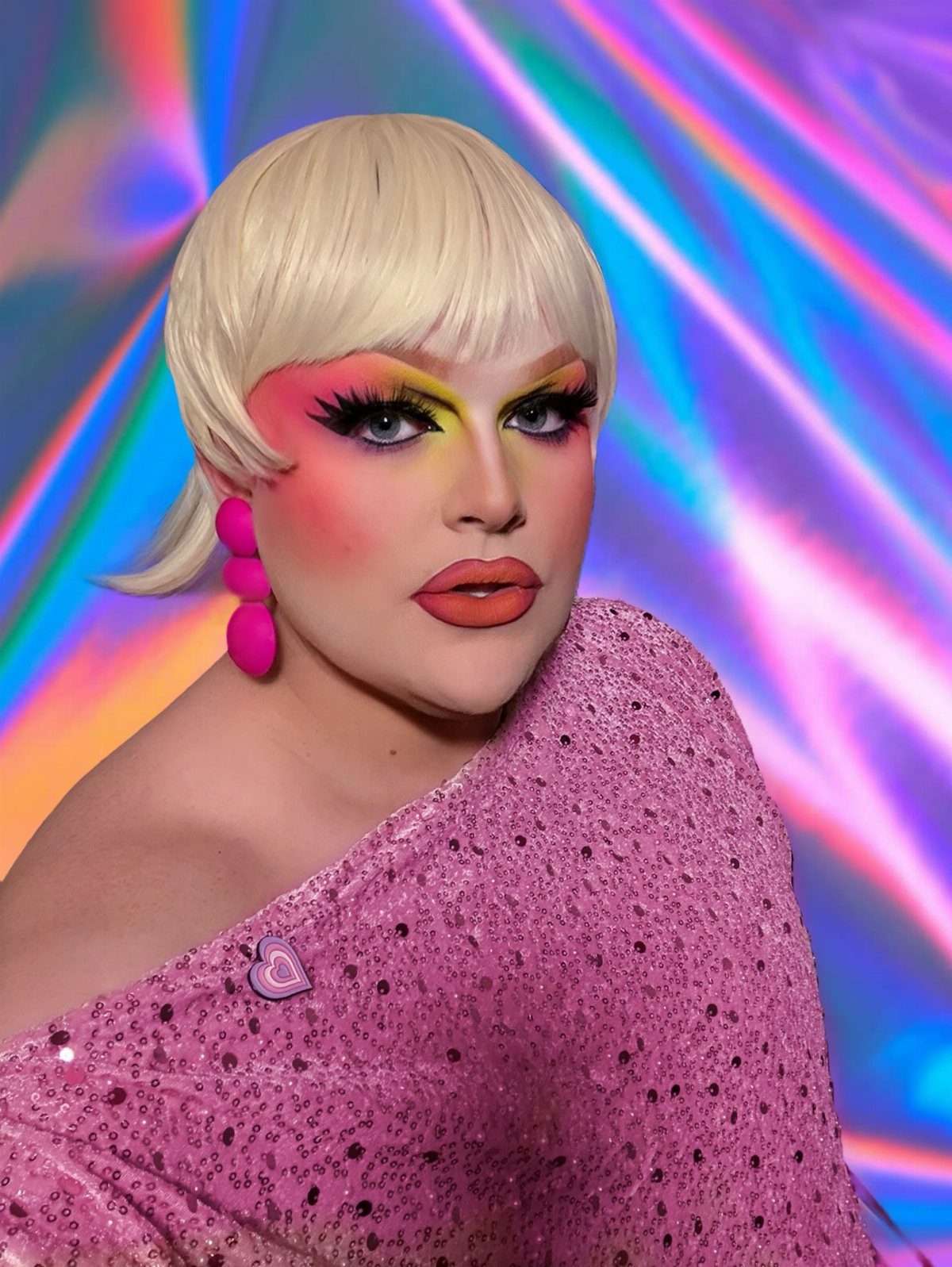 A person with blonde hair and dramatic colorful makeup wearing a pink sequined top.