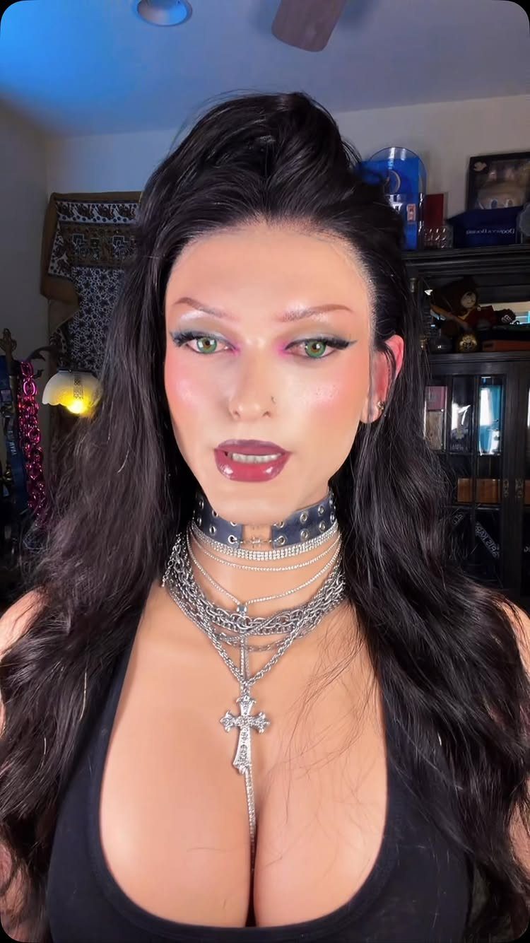 A woman wearing dramatic makeup and multiple layered silver necklaces with a large cross pendant.