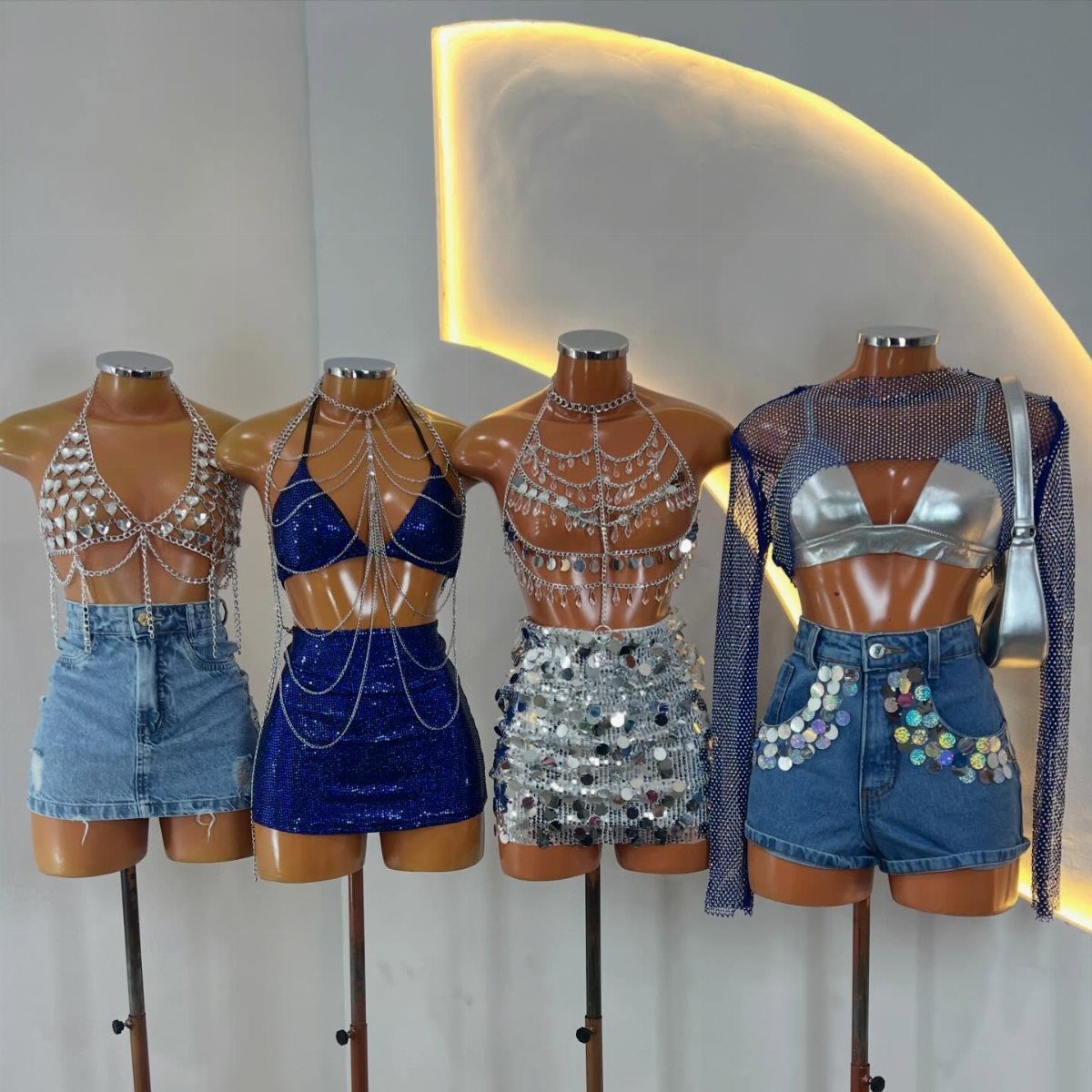 Four mannequins showcasing various sparkling rave outfits with chains, sequins, and denim shorts.