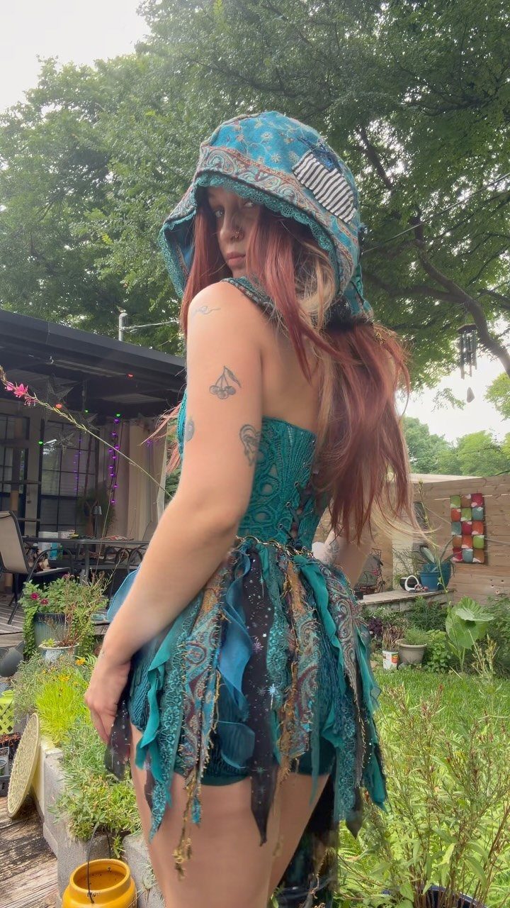 Woman in a teal patterned fairy-style outfit posing in a garden.