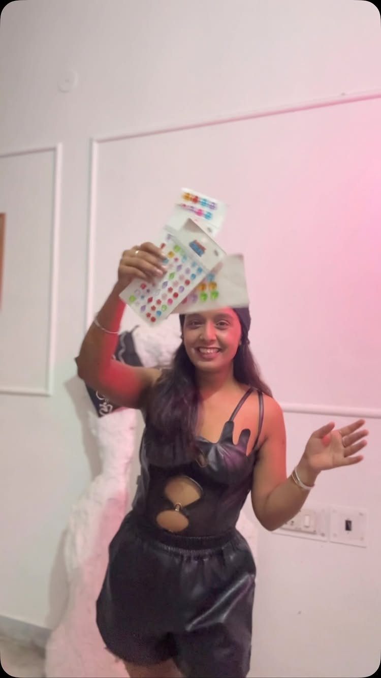 Smiling woman in a black romper holding up colorful rhinestone sheets.