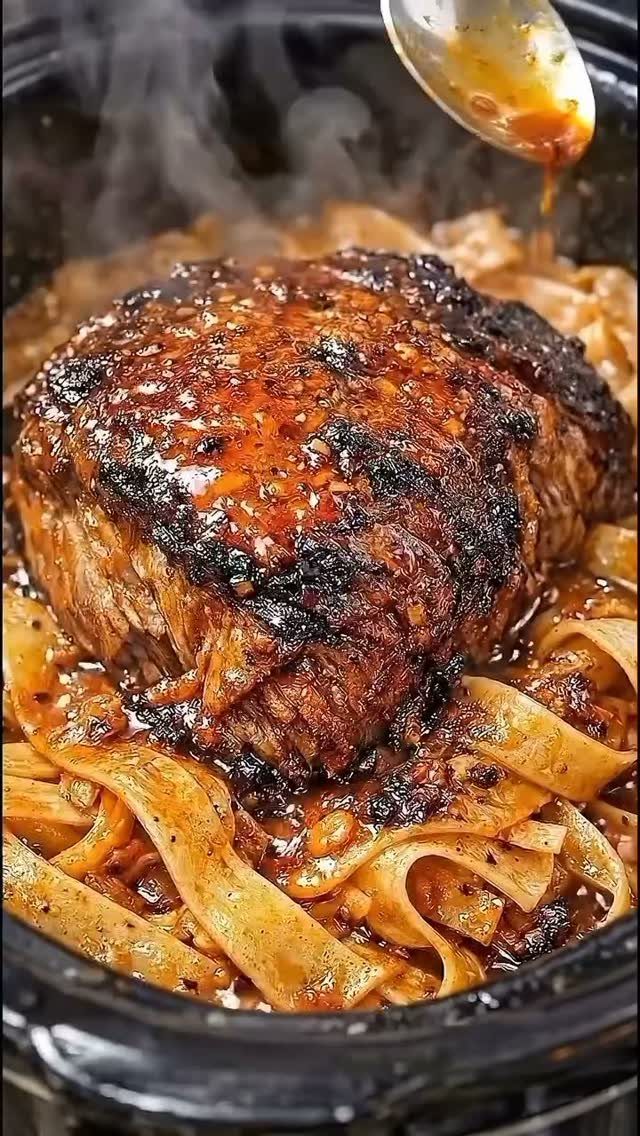 Seared beef resting on a bed of wide noodles in a steaming pot.