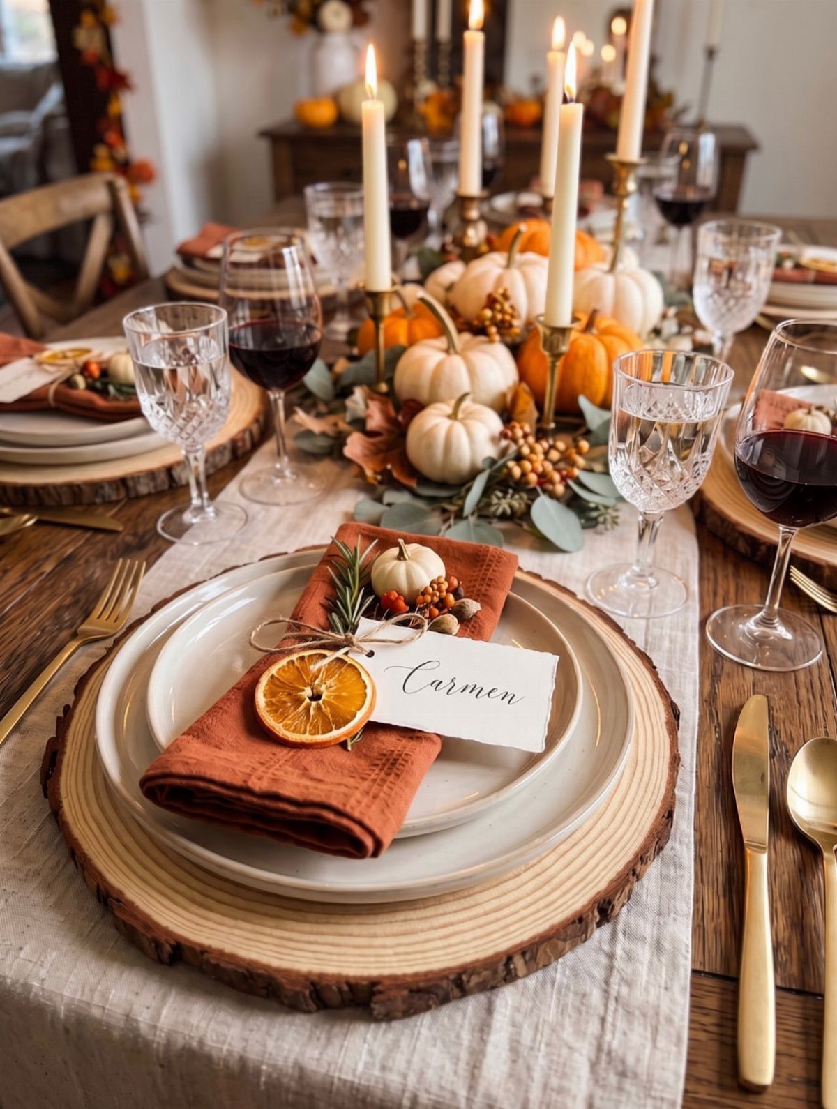 A decorated fall dinner table with pumpkins, lit candles, wine, and elegant place settings.