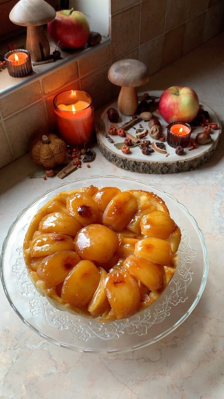 An apple tarte tatin on a glass plate with rustic fall decorations in the background.