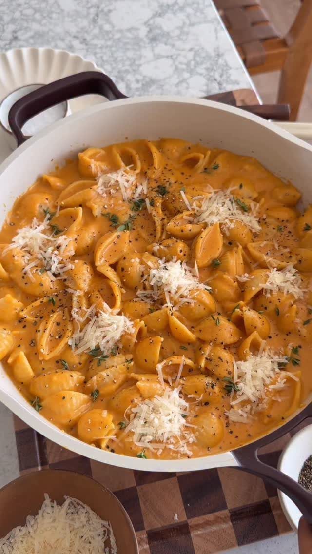 Creamy pumpkin shell pasta topped with shredded parmesan cheese in a white skillet.