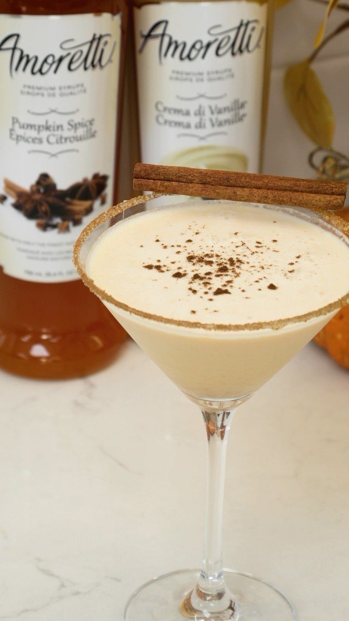 A creamy pumpkin spice cocktail in a martini glass with cinnamon sticks and a sugar rim.