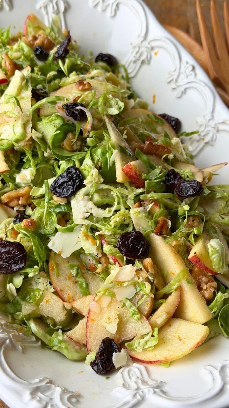 Shaved Brussels sprouts salad with sliced apples, walnuts, and dried cranberries in a white platter.