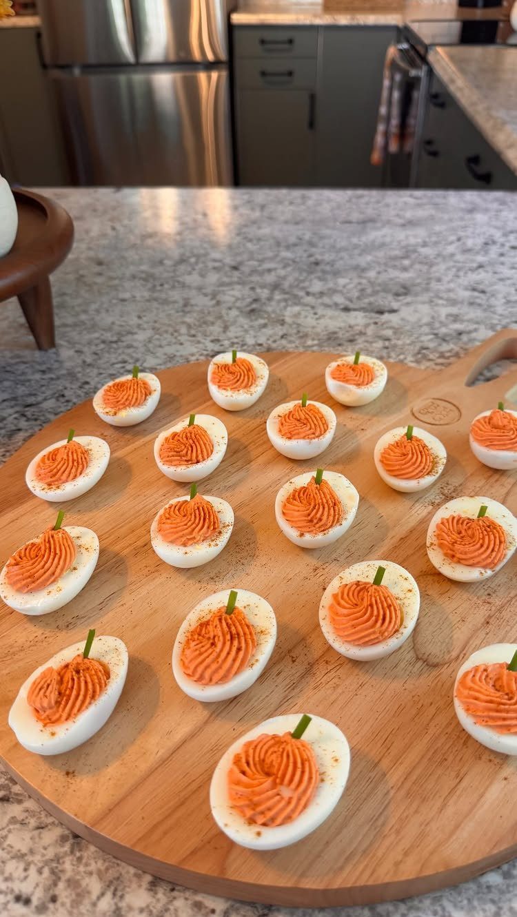 Deviled eggs with orange pumpkin-shaped filling and green stems on a wooden board.
