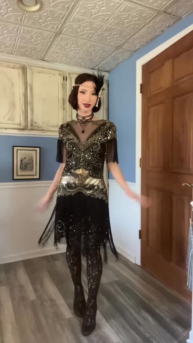 A woman posing in a black and gold sequined flapper costume with fringe and a headband.
