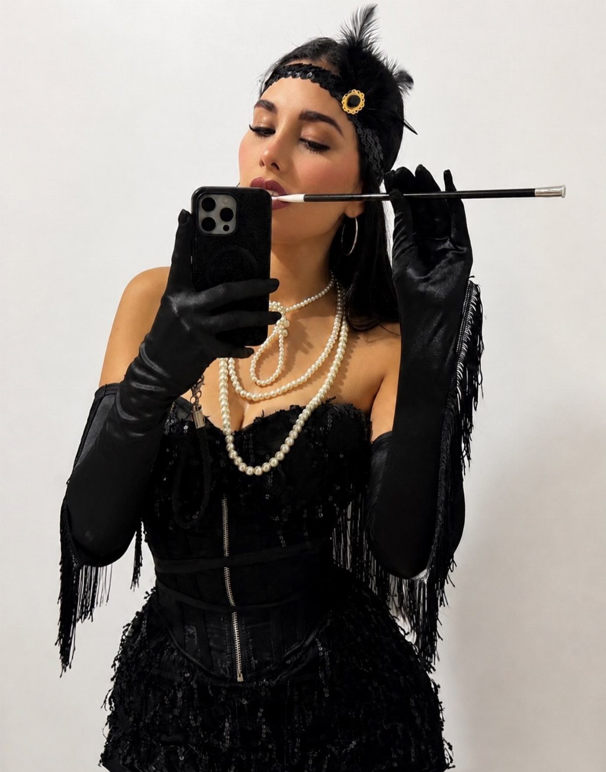 Woman in a black sequined flapper costume with pearls and long gloves taking a selfie.