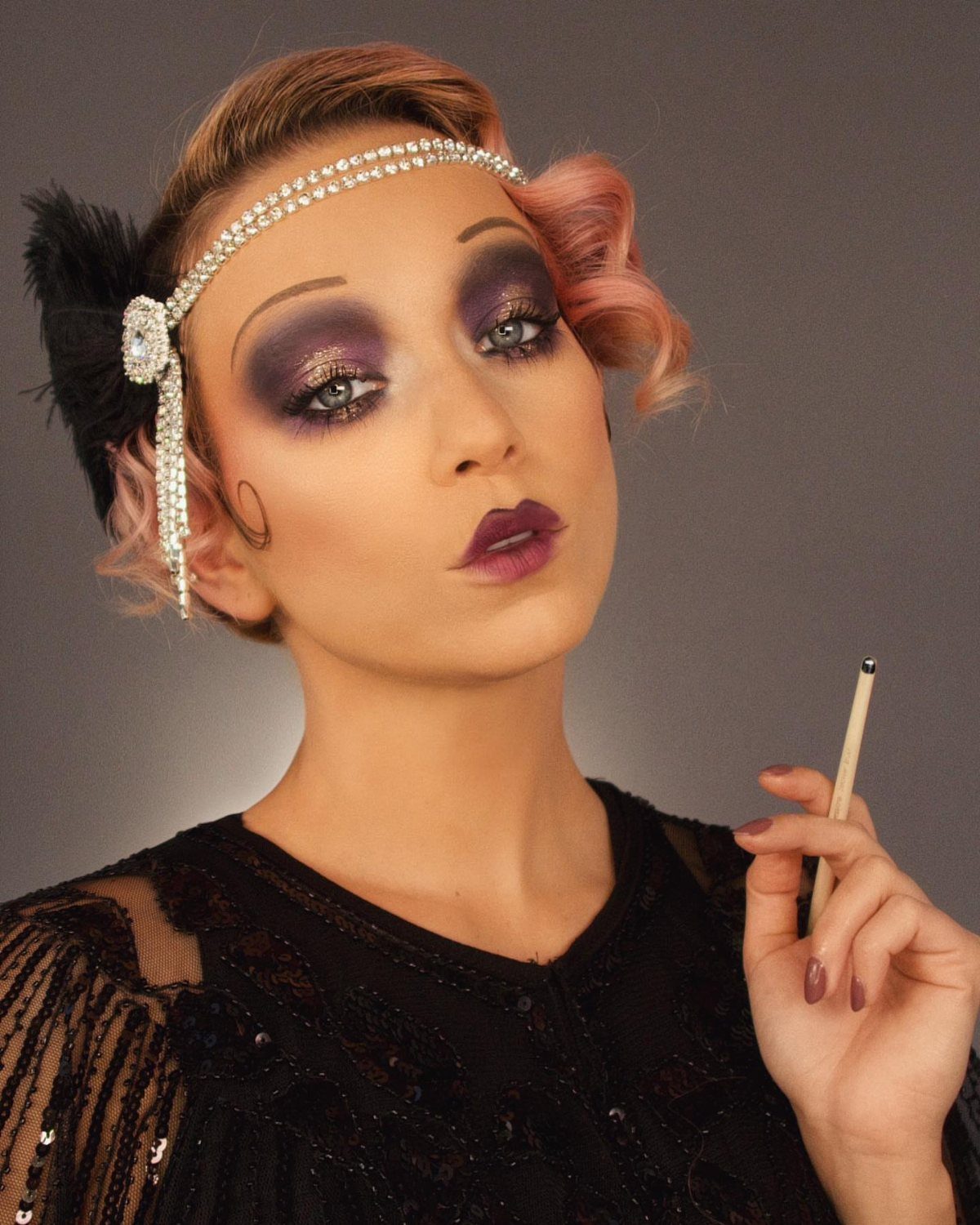 Woman with dramatic purple glitter eyeshadow and dark plum lipstick wearing a rhinestone headband.