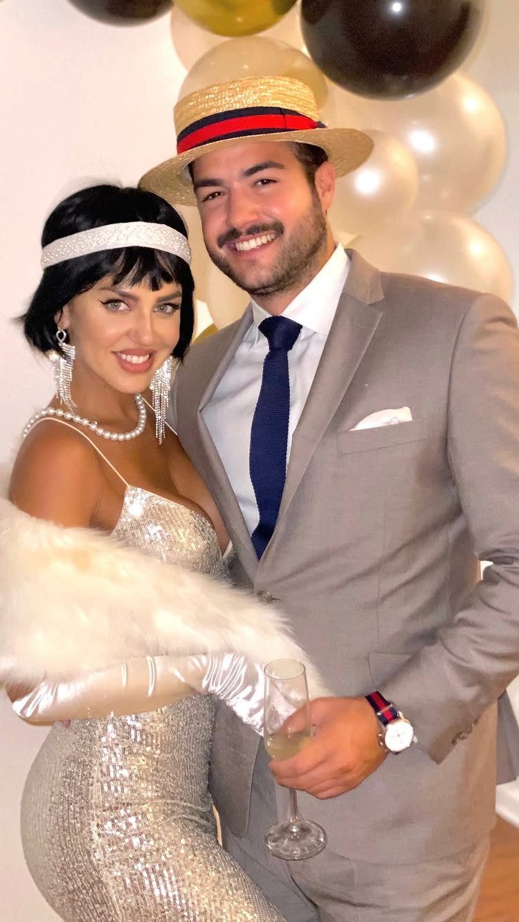 A man in a suit and a woman in a silver flapper dress posing together.