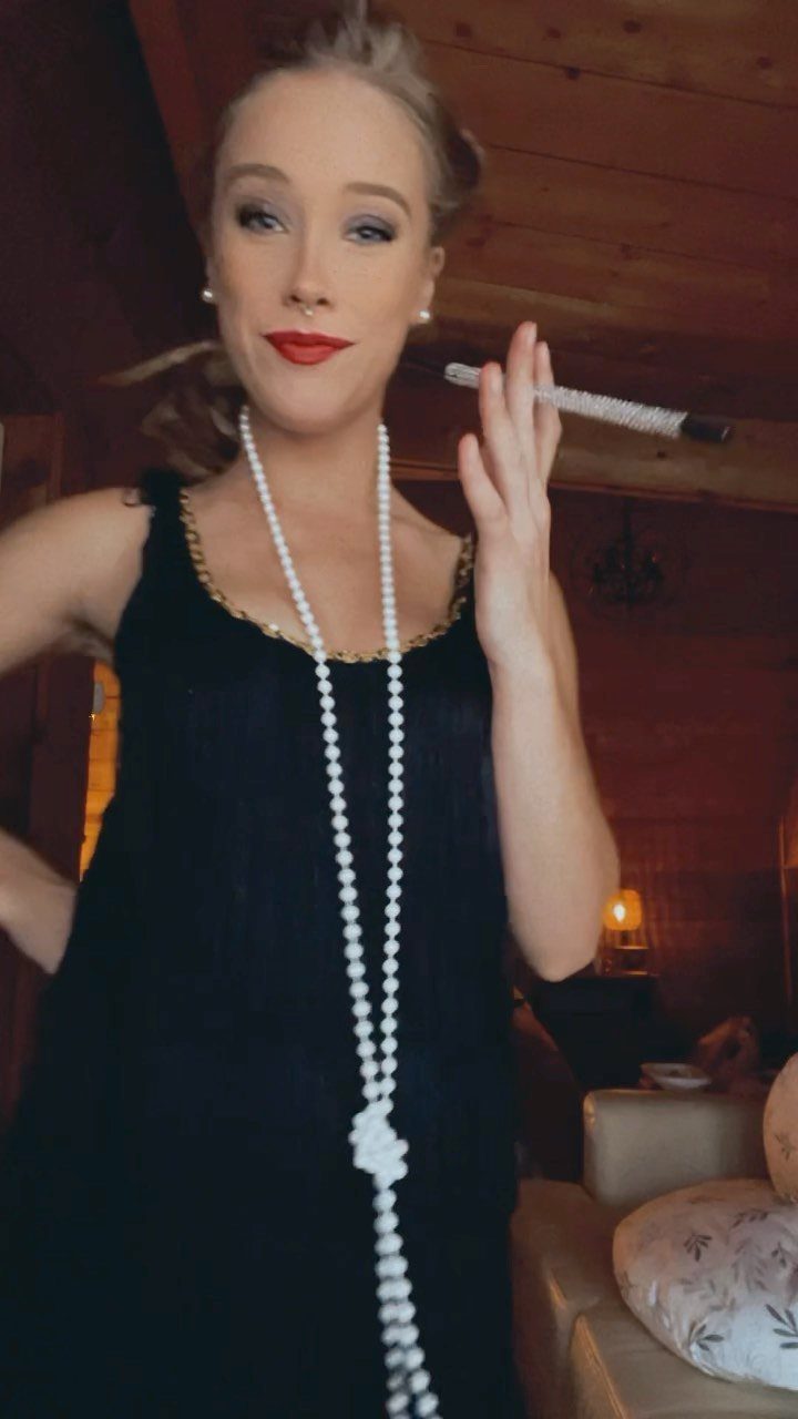 Woman in a black flapper dress with long pearl necklace holding a cigarette holder.