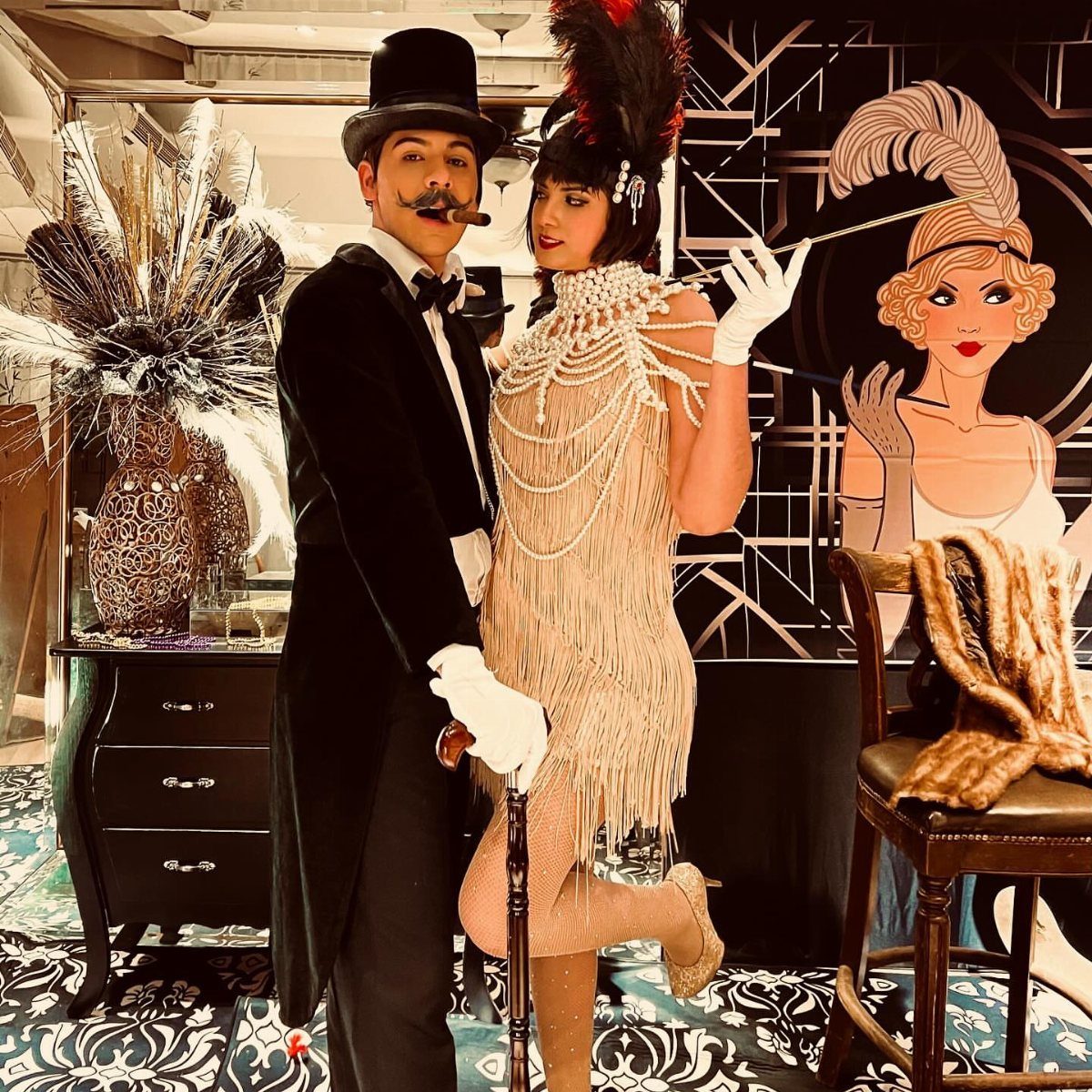 A man in a tuxedo and a woman in a fringed flapper costume posing together.