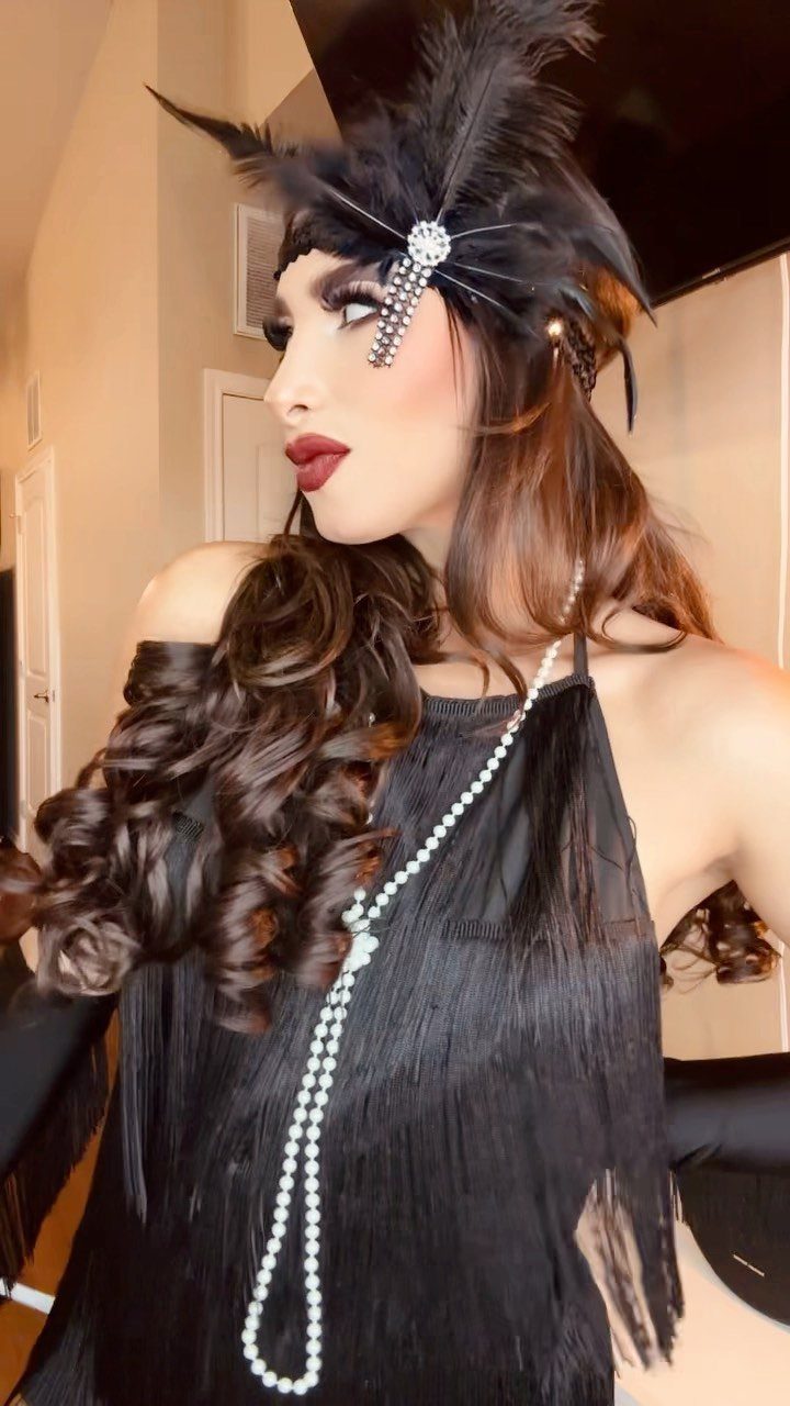 Woman wearing a black fringe flapper dress with a feathered headband and pearl necklace.