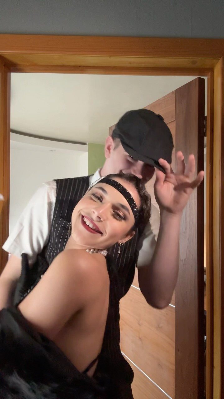 A smiling woman wearing a black flapper headband poses with a man in vintage attire.