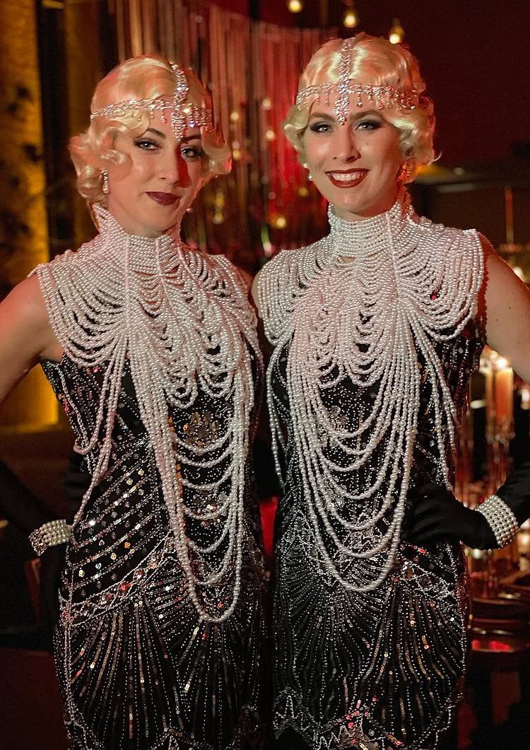 Two women wearing matching black and pearl 1920s flapper costumes and headbands.