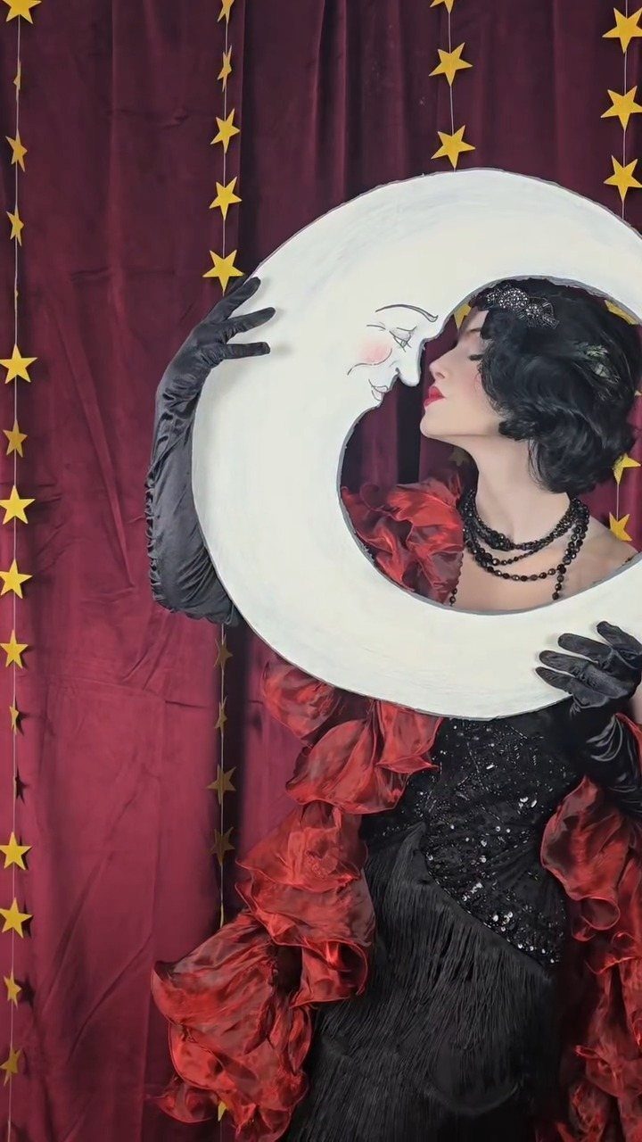 Woman in a black and red ruffled flapper costume posing behind a large crescent moon prop.