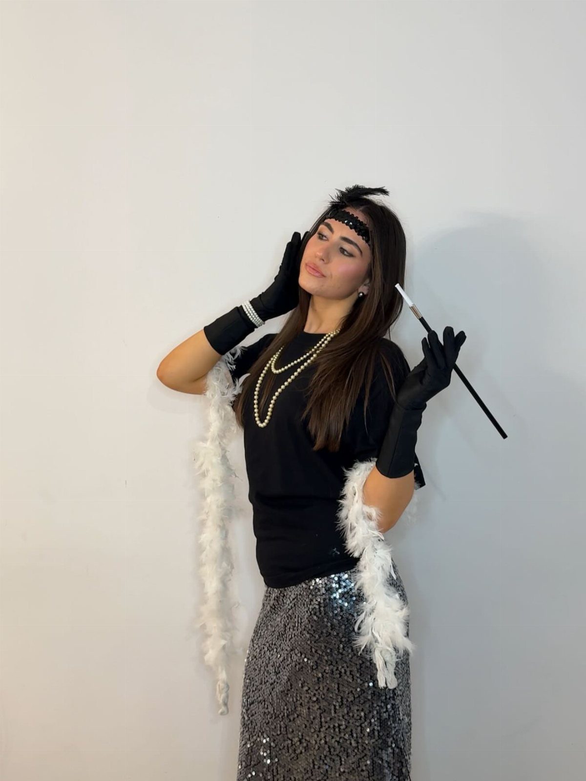 A woman dressed in a flapper costume with sequins, pearls, and long black gloves.