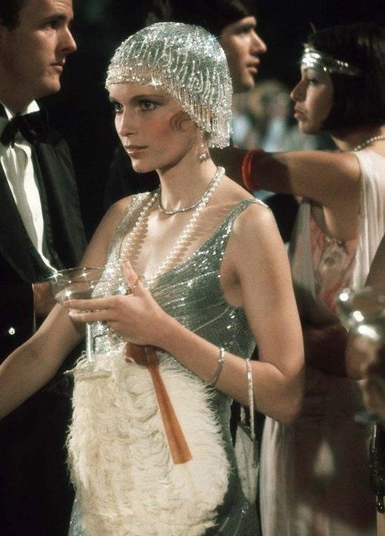 Woman wearing a silver sequined flapper dress and beaded hat holding a cocktail glass.