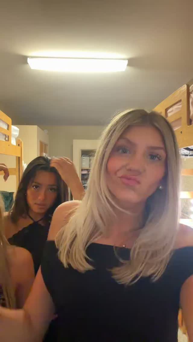 Two young women posing in black tops inside a dormitory room with bunk beds.
