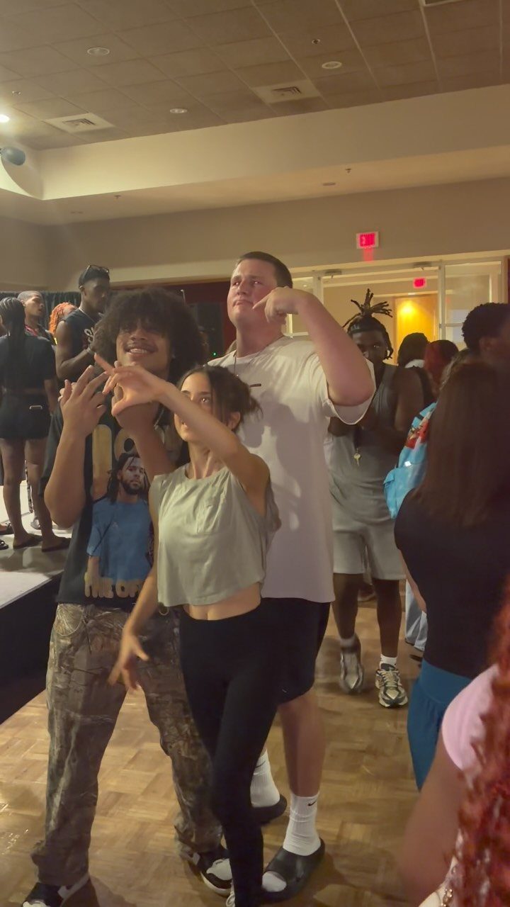 Young adults dancing together in a crowded, dimly lit indoor social gathering space.
