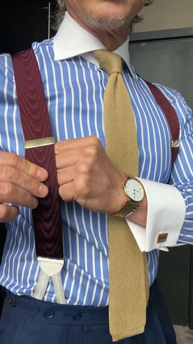 Man in a striped shirt, gold tie, and burgundy suspenders adjusting his attire.
