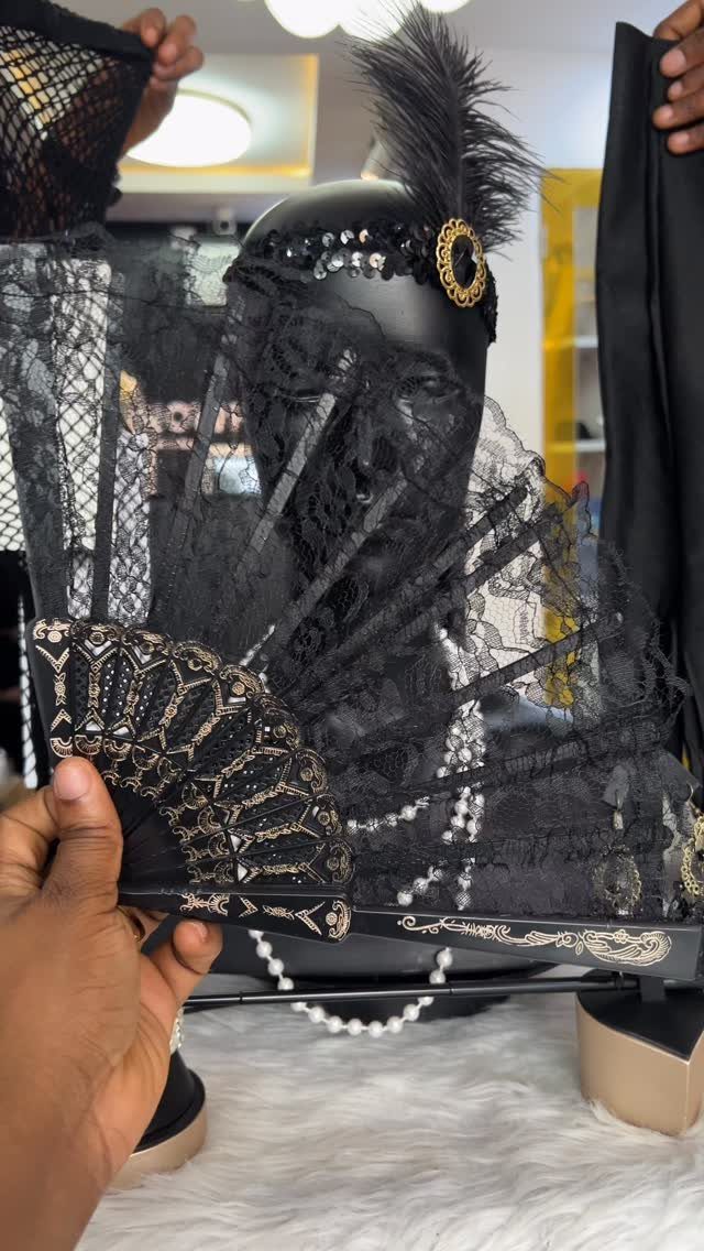 A black lace fan with gold details held before a mannequin wearing a feathered headband.