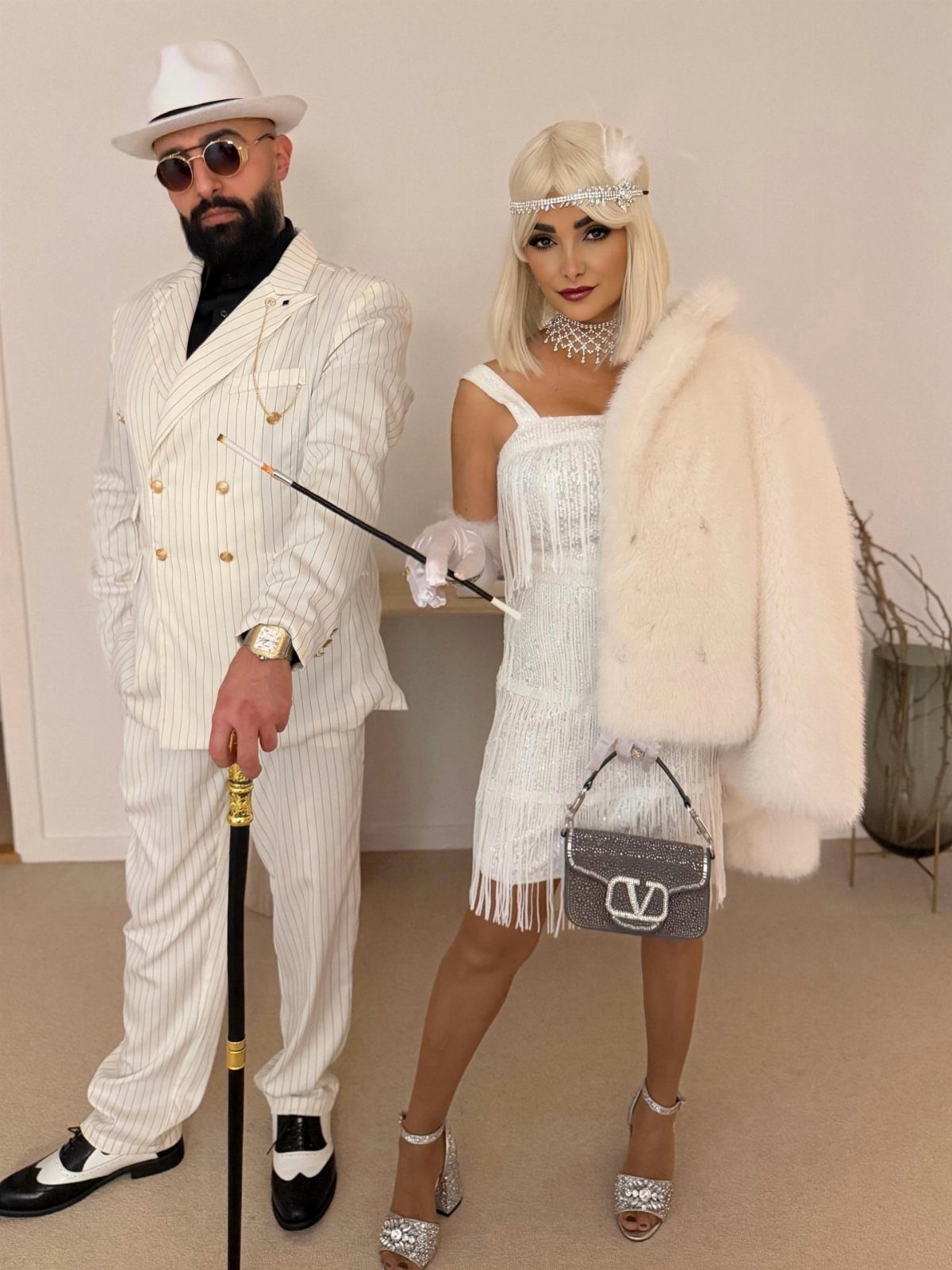 A man and woman dressed in white 1920s Gatsby-style costumes posing together.