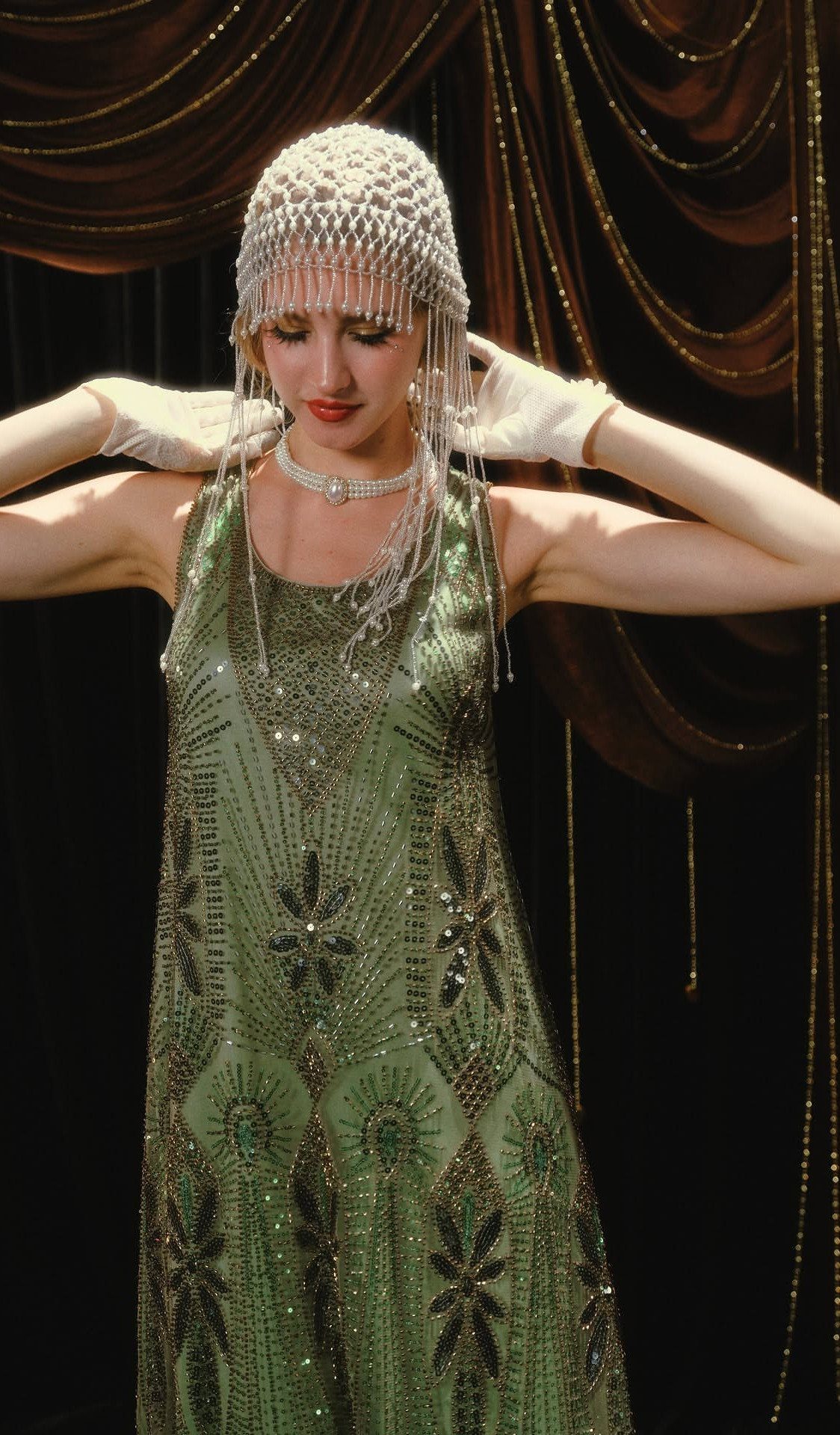 Woman in a green beaded Art Deco flapper dress and matching headpiece.