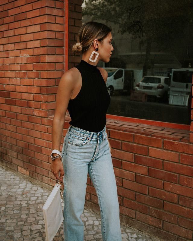 Woman wearing large white rectangular statement earrings, a black halter top, and light blue jeans.