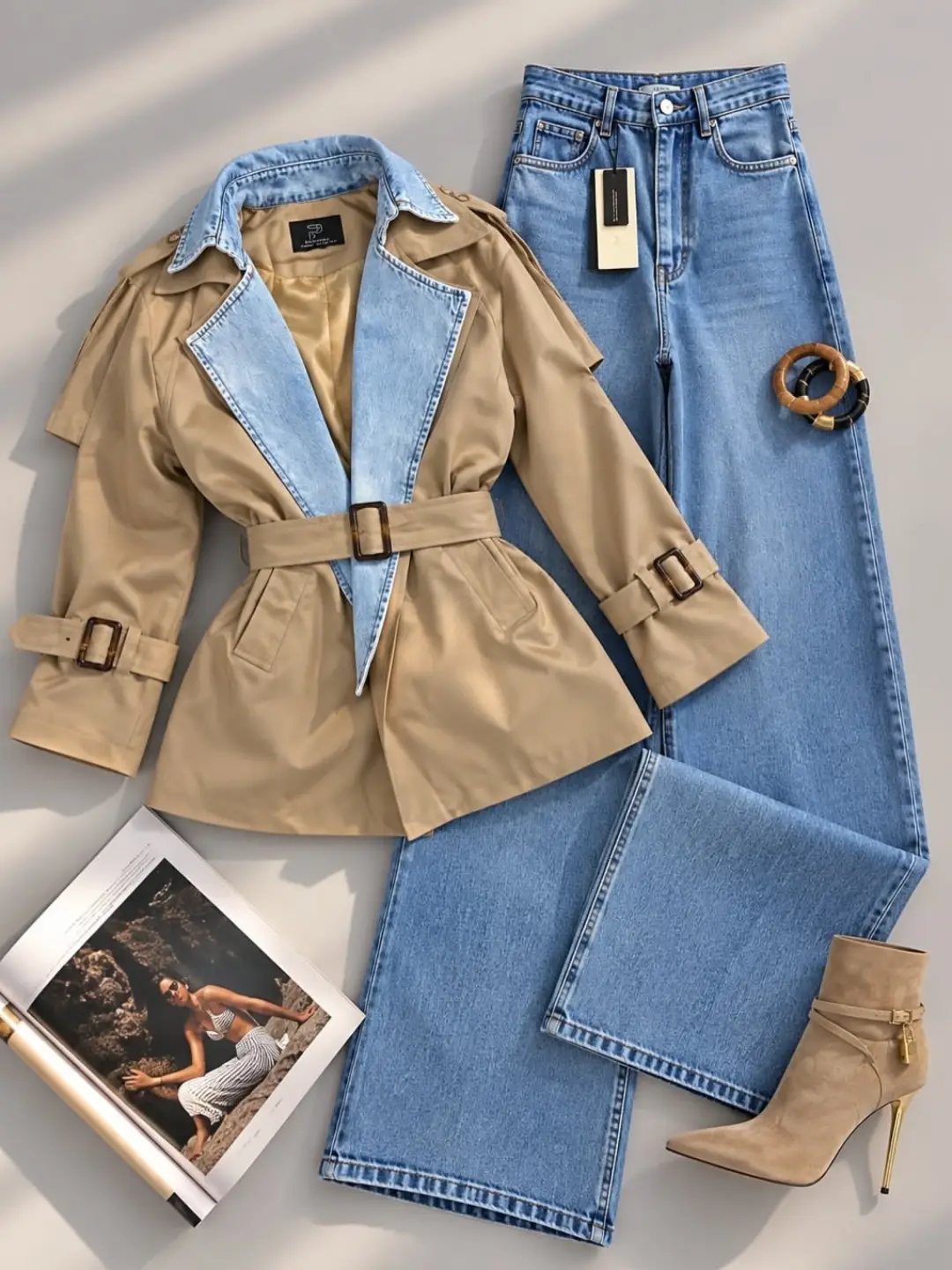 Tan trench coat with denim lapels, blue jeans, and tan boots laid out on a grey background.