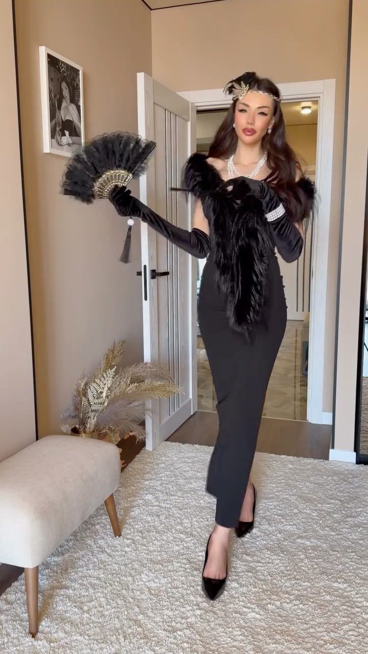 Woman in black formal dress, long gloves, and feather accessories posing in a room.