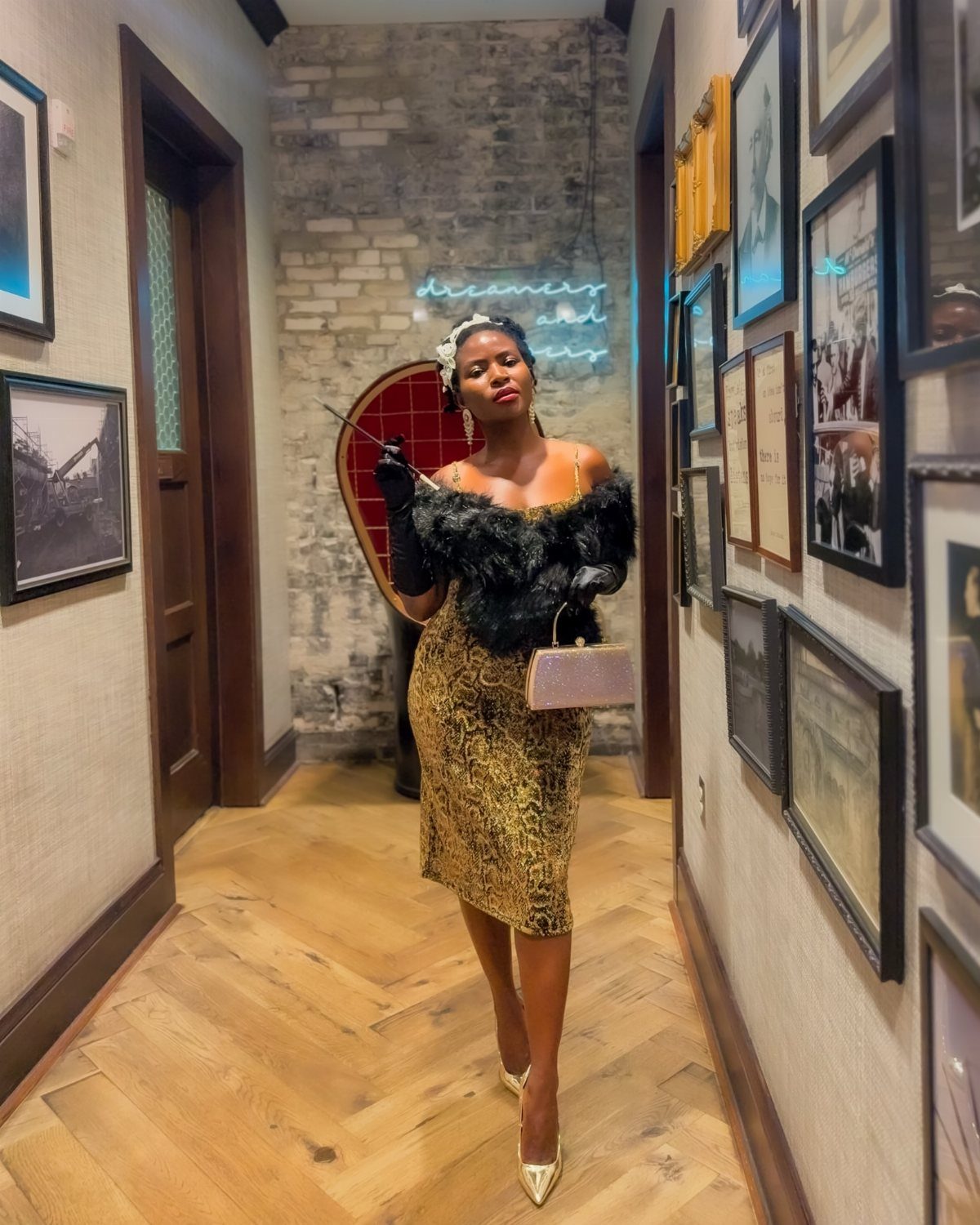 Woman in gold sequined dress and black fur shrug posing in a hallway.
