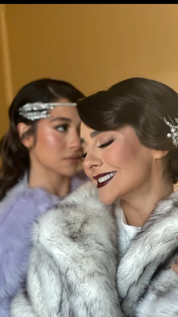 Two women showcasing vintage Gatsby-style hair and makeup with dark red lipstick and silver headbands.