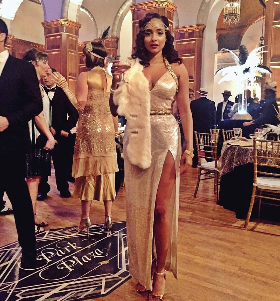 Woman in a gold sequined gown and white fur stole posing in a grand ballroom.