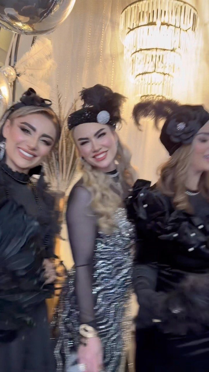 Three women smiling while wearing 1920s flapper style costumes and feathered headbands.