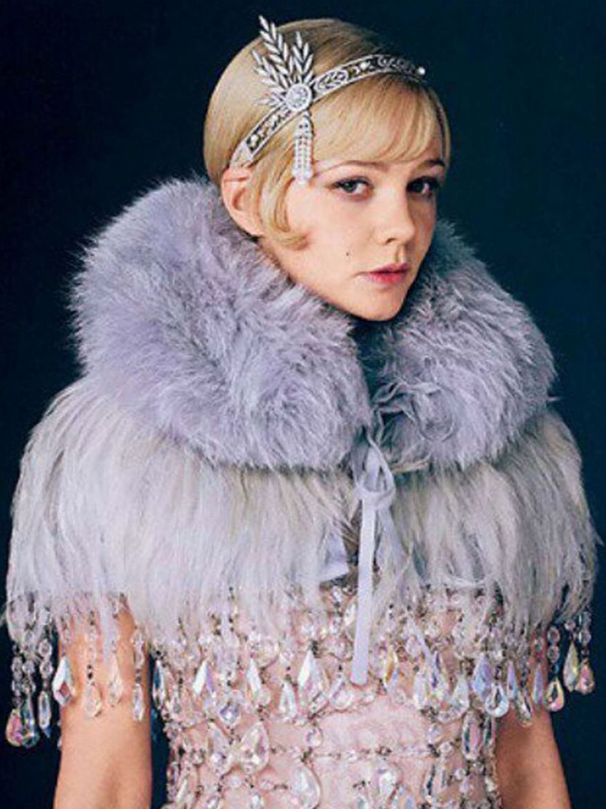 A woman wearing a silver beaded headband and a grey fur stole with a crystal dress.