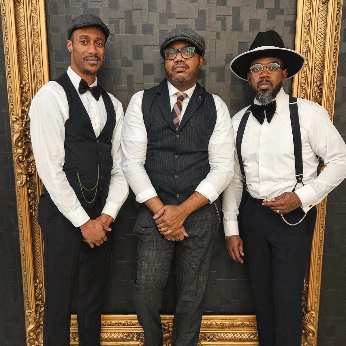 Three men posing in vintage gangster-style clothing including waistcoats, hats, and suspenders.