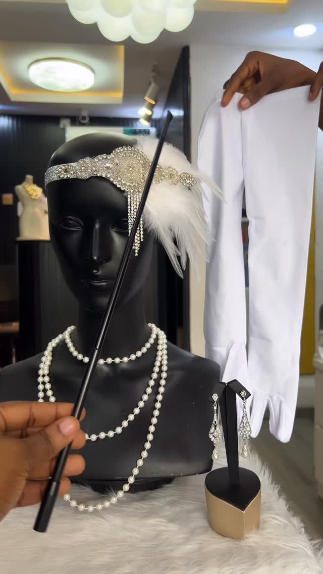 Mannequin head wearing a beaded Art Deco headband with feathers and layered pearl necklaces.