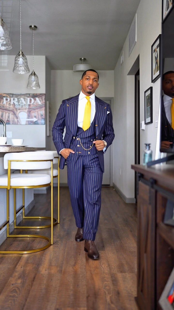 A man wearing a navy blue pinstripe three-piece suit with a yellow tie and gold pocket watch chain.
