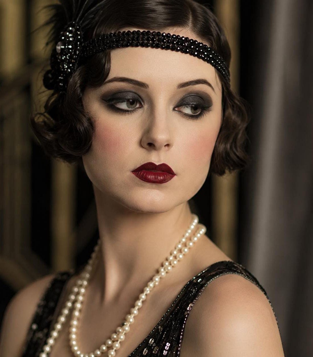Woman with dark finger wave hair, smoky eye makeup, and red lipstick wearing pearls.