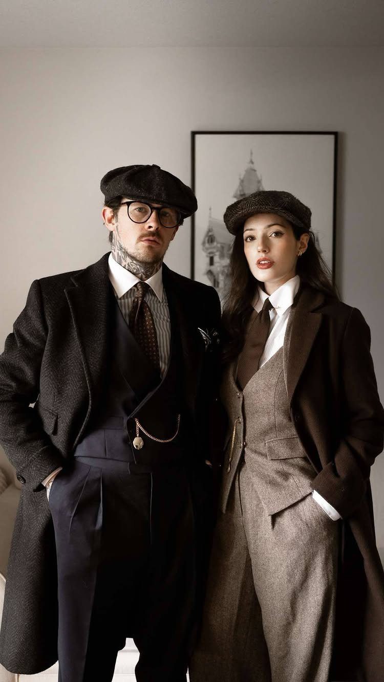 A man and woman posing in vintage 1920s inspired formal attire and flat caps.