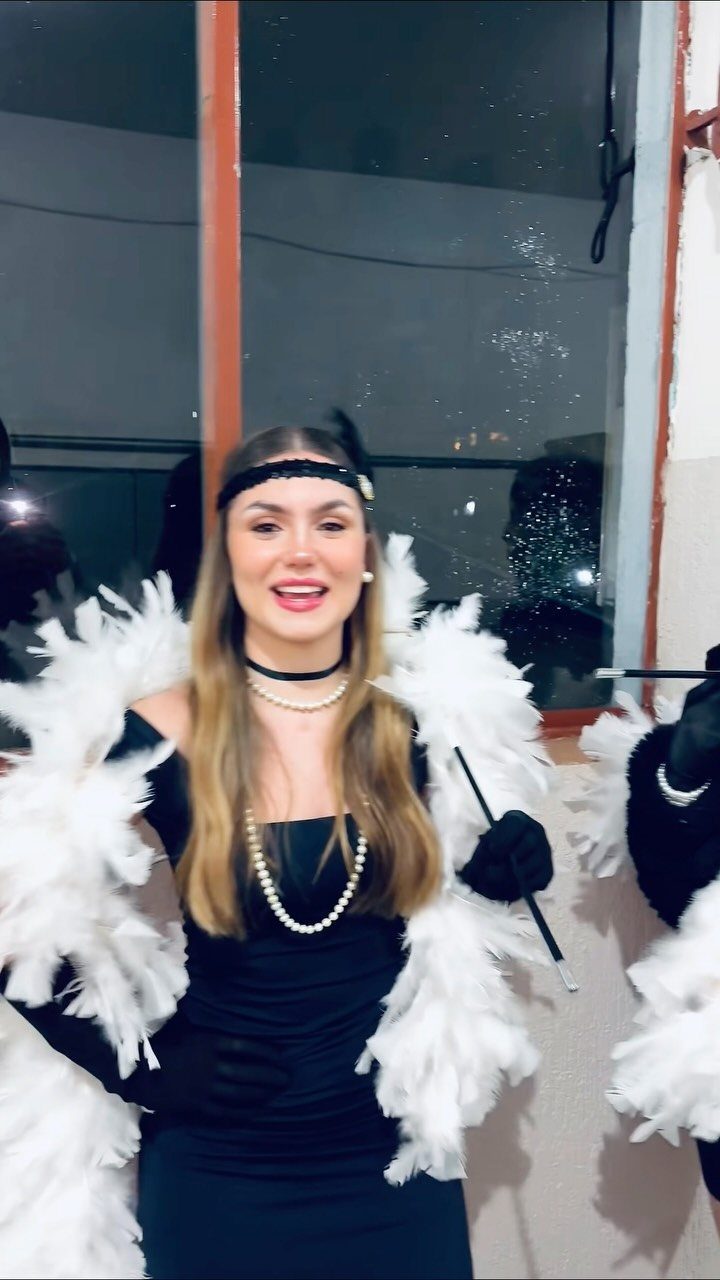 A woman wearing a black dress and white feather boa with pearl accessories.