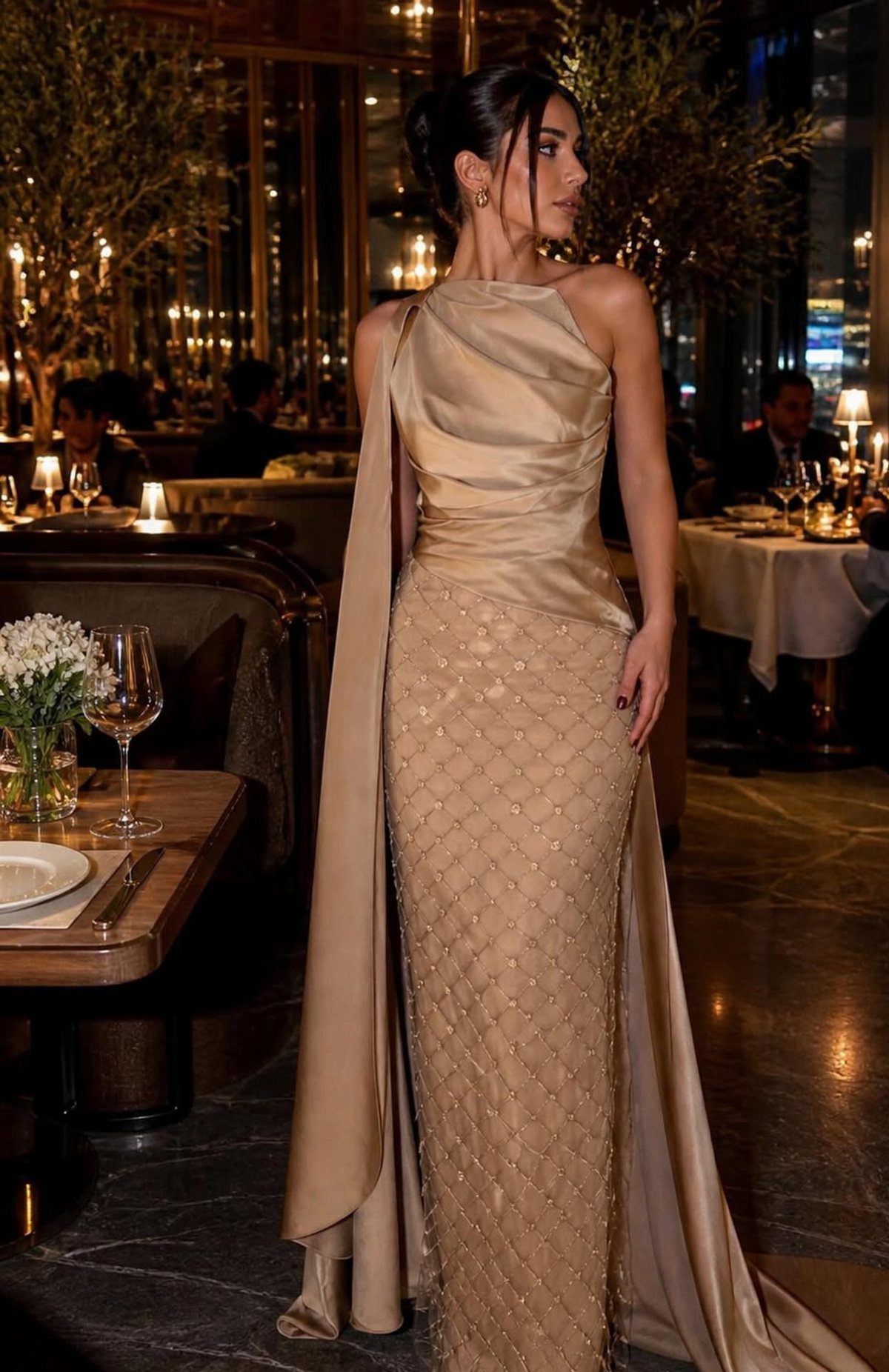 Woman in a champagne one-shoulder mermaid gown with beadwork standing in a restaurant.