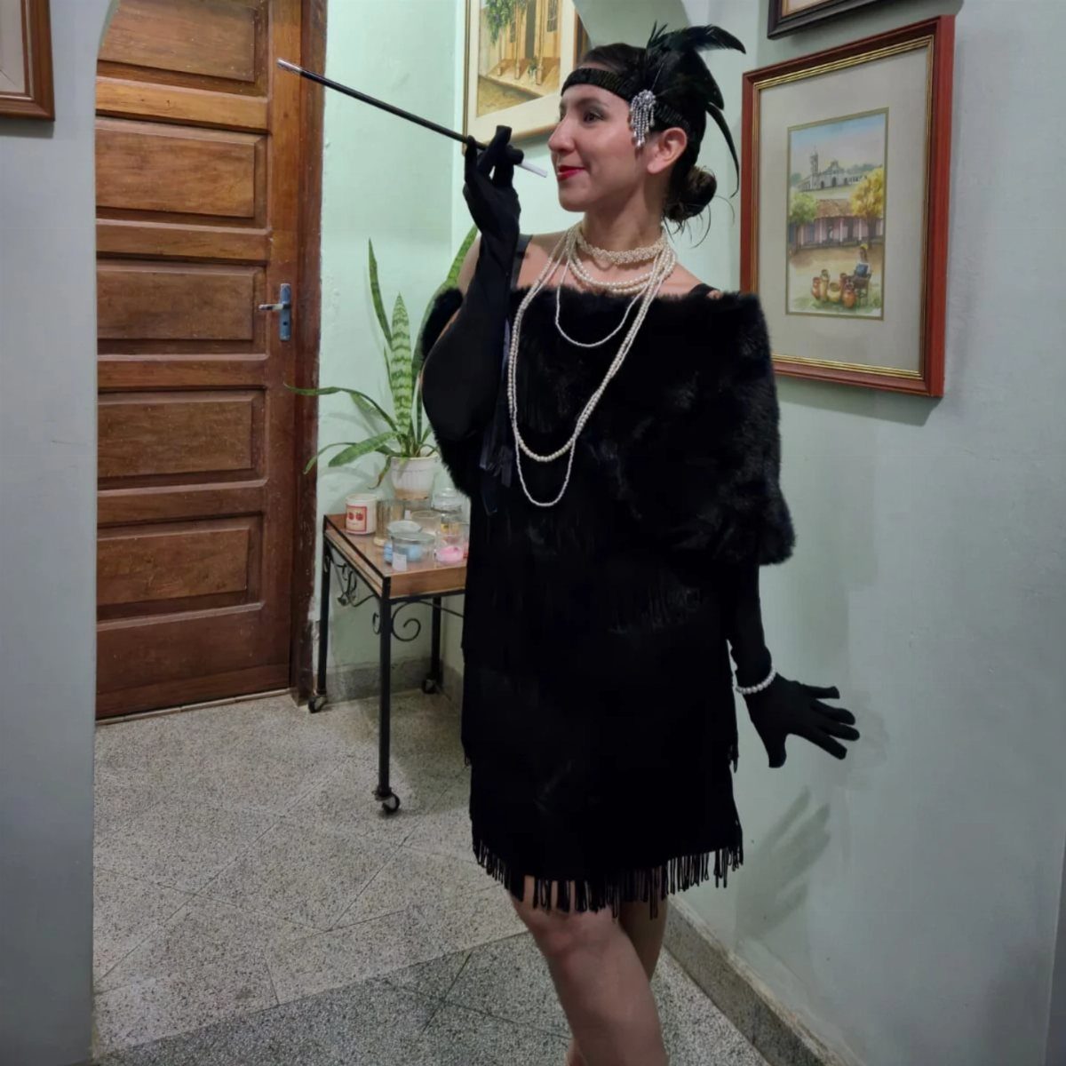 Woman in black flapper dress, long gloves, and pearls holding a cigarette holder.