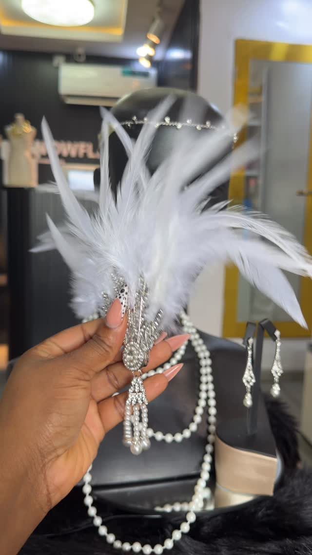 White feathered headband with silver jewels, pearls, and earrings displayed on a black mannequin head.