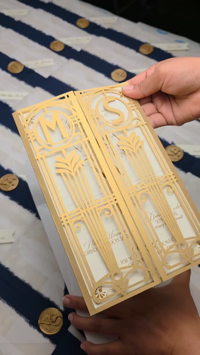 Hands holding a gold laser-cut Art Deco style invitation with geometric patterns.