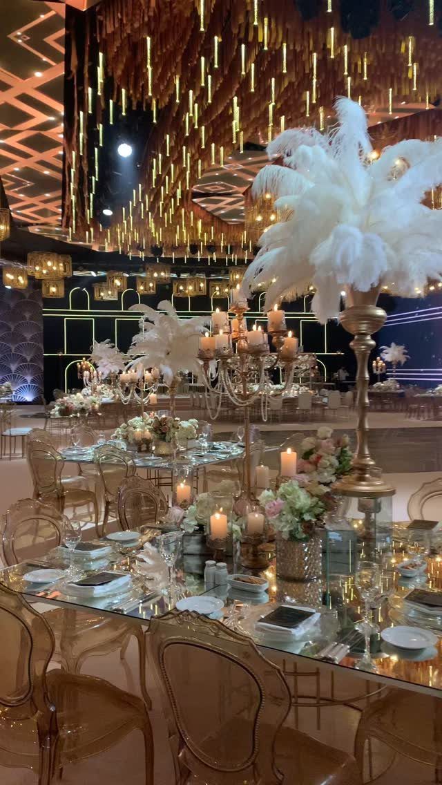 White feather centerpieces in gold candelabras on elegant banquet tables with candles and flowers.